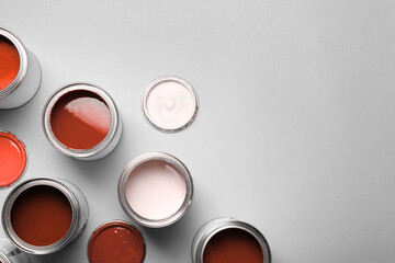 Cans with paint in shades of red on light grey background, top view. Space for text