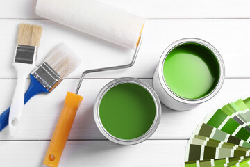 Cans with paint in shades of green, color palette, roller and brushes on white wooden background,...