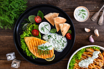 Grilled chicken breast, pita bread and tzatziki sauce on wooden table. Greek style food
