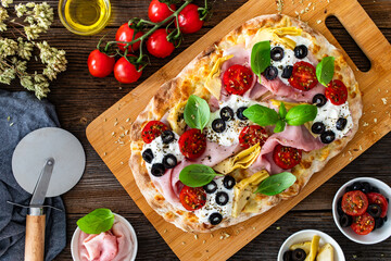 Pinsa Romana with mozzarella and burrata cheese, boiled ham, artichoke, cherry tomatoes, black...