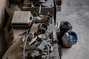 A cluttered workbench holds a black toolbox, worn work boots, tangled scrap metal parts, discarded...