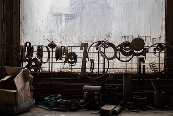Various greasy metal parts hang from a wire mesh against a dirty window, with more tools and...