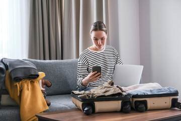 Woman packing suitcase at home while working on laptop. Concept of digital nomad lifestyle, remote job, travel, freedom, relocation and slow living. Modern flexible work and mobility.