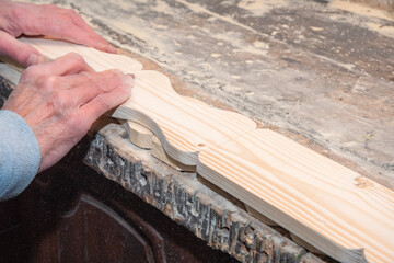 Professional carpenter performs the final sanding of a decorative board with his bare hands using...