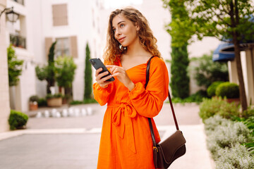 Beautiful woman with a phone and in a bright dress walks along the beautiful streets of the city. A...