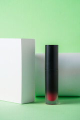 Mockup of black blank thin tube - mascara, lip gloss, gel, eyeliner, oil, etc. Cosmetic package with stylish props on green background. 