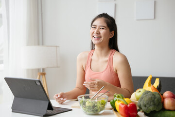 Healthy woman preparing organic fruit and vegetable salad in kitchen for healthy lifestyle during video calling and live streaming via tablet on social media