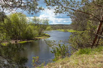 River landscape and green forest with trees blue water clouds on sky, full-flowing river in spring.