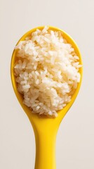 Scoop of white rice in a yellow spoon against a neutral background