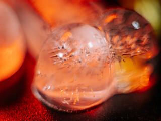 Close-up of a yellow flower beside two melting ice shapes on a vibrant red and black surface with glowing reflections. Copy space.