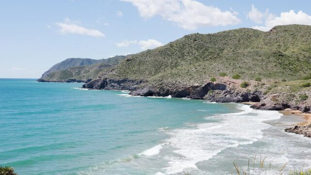 Cliffside Coastal View of Calblanque Natural Park in Murcia, Spain with Rocky Hills, Vibrant Blue Sea, and Rolling Waves on a Sunny Day