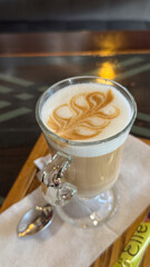 Elegant cappuccino with intricate latte art in a clear glass on wooden tray captures serenity and sophistication in every sip