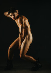 Naklejka premium A muscular man posing dramatically under low key lighting, emphasizing form and emotion.