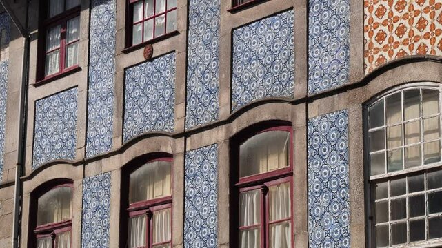 Traditional Portuguese Blue tiled facade with stone frames and arched maroon window frames under direct sunlight