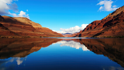 Naklejka premium Stunning landscape depicting a calm lake reflecting majestic cliffs and a vibrant blue sky under fluffy clouds