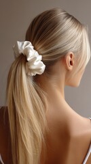 Elegant woman with long blonde hair styled in ponytail and white scrunchie during soft indoor lighting