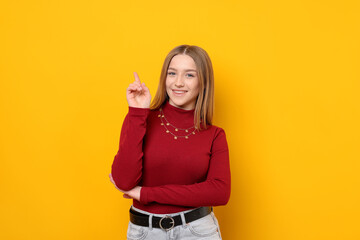 Portrait of smiling teenage girl pointing upwards on yellow background