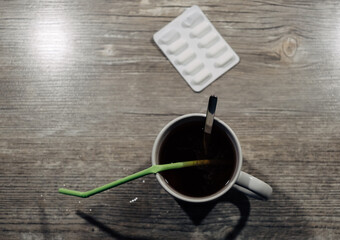 A cup of coffee with a green straw in it sits on a wooden table next to a pill b