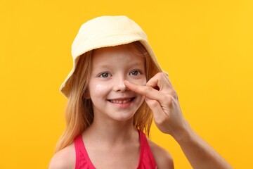 Mother applying sun protection cream onto her daughter's nose on yellow background, closeup
