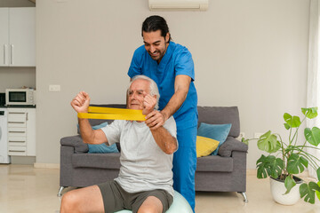 Senior man exercising with yellow resistance band and male physiotherapist on rehab ball at home