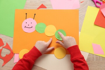 Little girl making handmade project with color paper at wooden table, top view