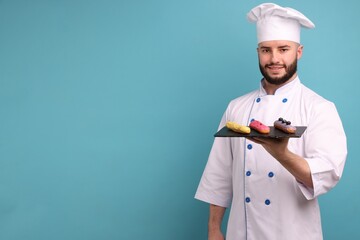 Happy confectioner in uniform holding delicious eclairs on light blue background, space for text