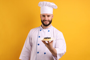 Happy confectioner in uniform holding tart with blueberries on orange background