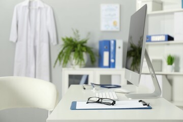 Doctor's workplace. Computer monitor, clipboard, stethoscope and glasses on white table in medical office