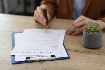 Obraz premium Woman stamping licensing agreement document at wooden table indoors, closeup