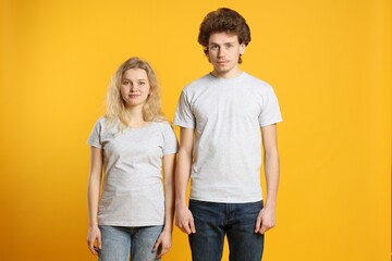 Young woman and man wearing blank white t-shirts on orange background. Mockup for design