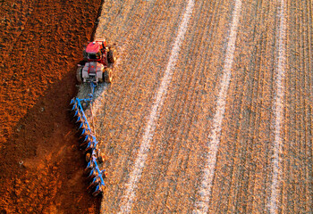Plowing field on sunset. Red Tractor with Plough on Plowed. Ploughing, Soil Tillage. Agricultural Tractor on Cultivation Field for Sowing Seeds. Grain deal, Tractor on Field Cultivating in Spring.