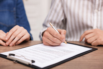 Man putting signature on document at wooden table, closeup