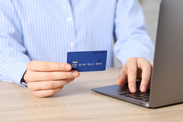 Online payment. Woman with credit card typing on laptop at wooden table, closeup