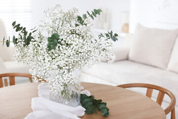 Bouquet of beautiful gypsophila flowers and eucalyptus branches in vase on table indoors