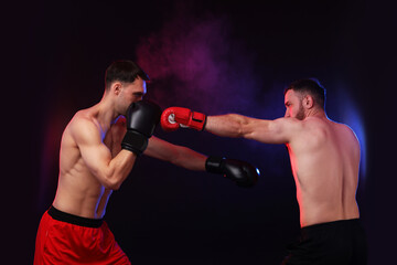 Men in boxing gloves fighting on dark background with smoke