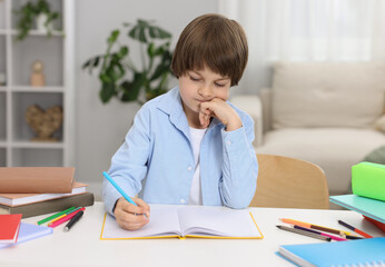 Cute little boy doing homework at table indoors