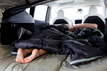 Obraz premium Feet peeking from sleeping bag inside car bed during road trip adventure