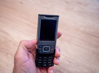 Close-up of an old silver and black slider mobile phone with keypad, held in a hand, with wooden...