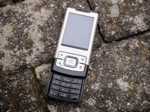 Old Nokia slider phone with physical buttons lying on stone pavement, close-up view from above.