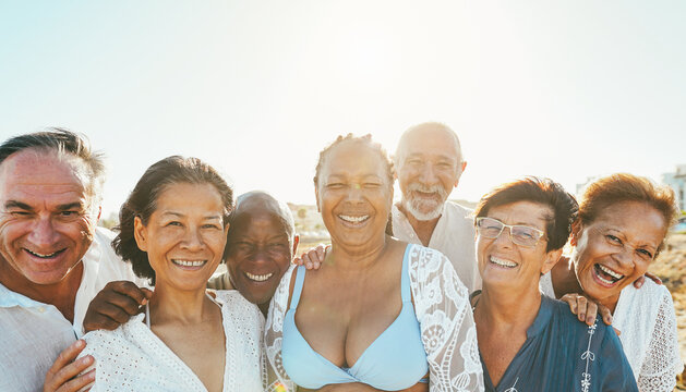 Happy senior people having fun walking on the beach at sunset wearing summer clothes - Joyful elderly lifestyle, vacation and travel concept - Main focus on center man face