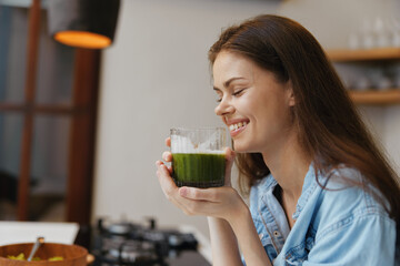 Young woman enjoying a green smoothie in a bright kitchen, showcasing a healthy lifestyle and joyful emotions for wellness themed content