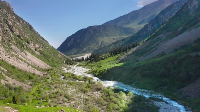 This footage depicts a peaceful creek running between two lush green mountains at Ala Archa National Park, Kyrgyzstan, a serene landscape.