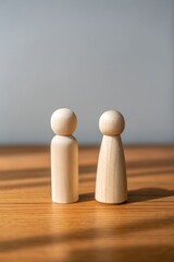Two simple wooden peg dolls standing close together on a wood table representing unity and connection