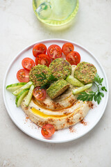 White plate with hummus, falafel, paprika and tomatoes, vertical shot on a light-beige stone background, selective focus