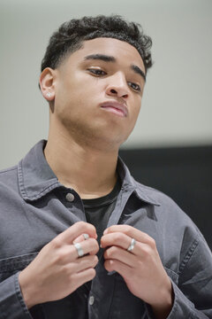 Beardless 18 year old Dominican man buttons his shirt. Teen fashion and self care habits