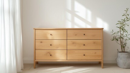 Wooden chest of drawers in a room with white walls and a window with white curtains. the chest is made of light-colored wood and has six drawers with black knobs.