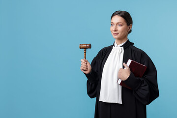 Judge with mallet and book on light blue background, space for text