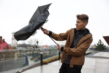 Man with broken umbrella fighting wind under rain outdoors