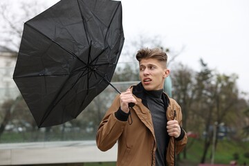 Man with broken umbrella fighting wind under rain outdoors