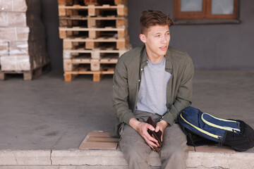 Man with empty wallet and backpack sitting on concrete floor outdoors. Financial problem